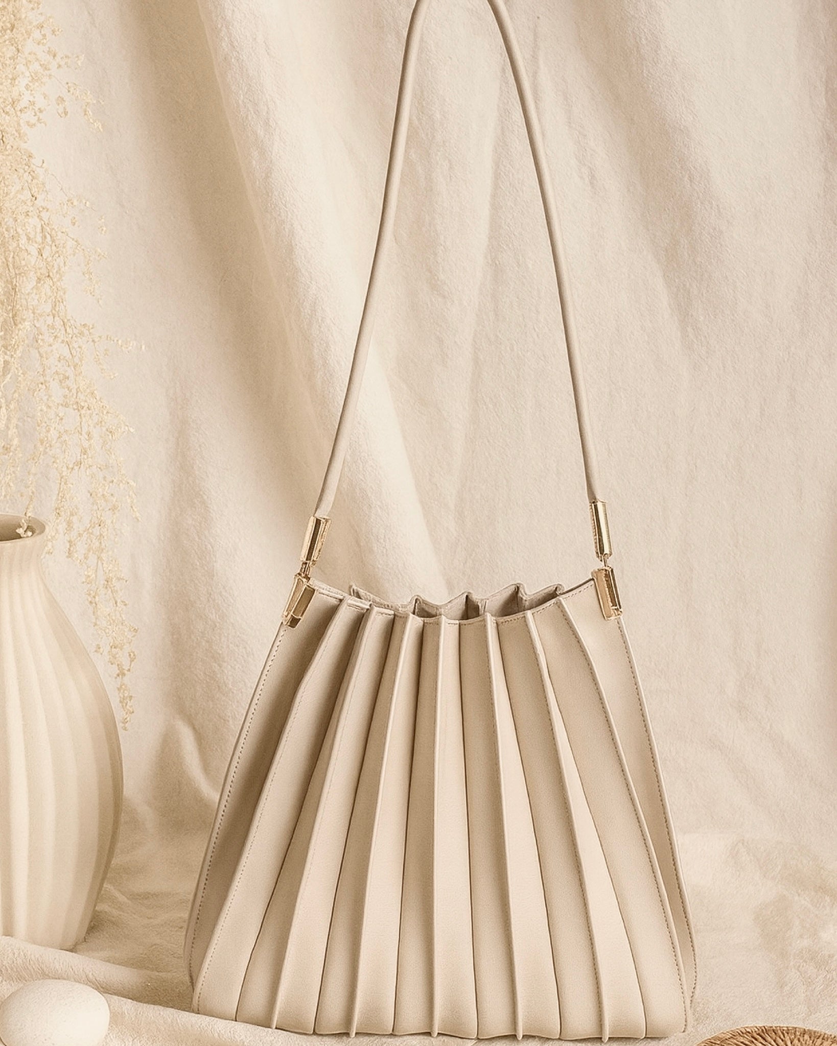 Beige pleated handbag with a chain strap on a textured beige background